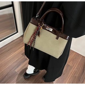 Detail of a two-tone handbag with silver twist-lock closure and woven lanyard ornament