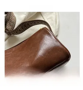 Détail de la texture cuir marron foncé et bandoulière tissée sur un sac oreiller