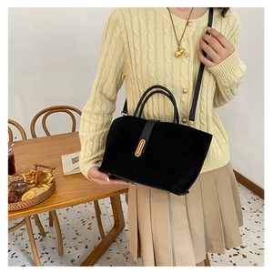 Detail showing elegant black suede crossbody bag with gold buckle on a model