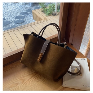 Detail of dark brown suede tote bag with leather handles and metal clasp on wooden ledge
