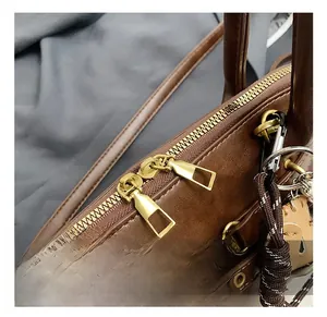 Close-up of golden hardware details and braided charm on a vintage brown leather handbag