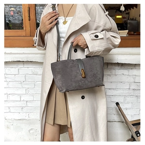 Detail of grey frosted suede tote bag with golden oval lock and leather handles