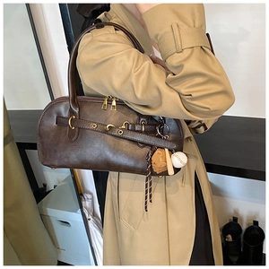 Detail of dark brown shell bag with baseball charms on a beige trench coat
