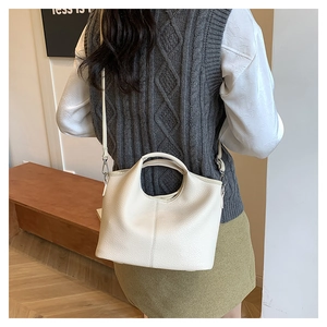 Detail of a creamy white litchi grain leather handbag with adjustable crossbody strap