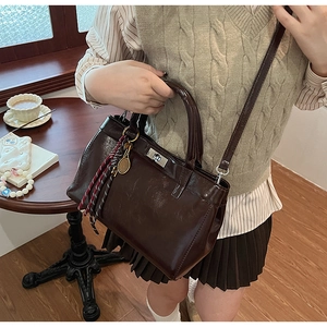 Détail d'un sac à main en cuir marron brillant avec fermoir rotatif et pompon