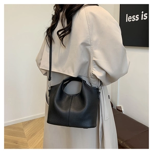 Detailed side view of a black pebble leather bucket bag on a minimalist beige trench coat