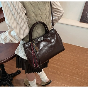 Détail du sac à main en cuir ciré marron foncé avec fermoir rotatif argenté et pompon