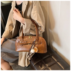 Close-up of brown vintage shell bag with gold hardware and baseball charm on a trench coat