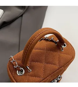 Macro detail of brown suede quilted mini bag featuring thick round handle and chain strap