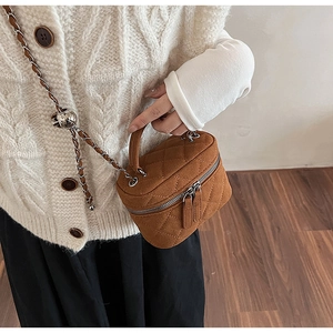 Detail of brown quilted suede crossbody bag with gold chain and top handle on model