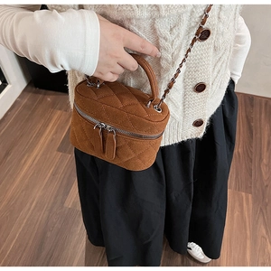 Close-up of brown quilted suede mini bag with gold chain strap worn on white sweater