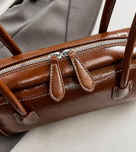Close-up of smooth dual metal zippers and white contrast stitching on a brown leather bag