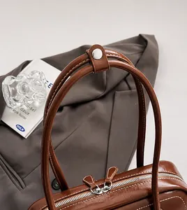 Detail of glossy brown leather handbag featuring silver metal zipper and round handles