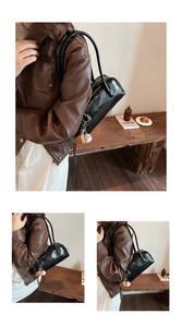 Detail of black glossy baguette bag with baseball charm and sleek zipper closure
