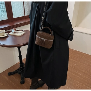 Detail of brown quilted suede mini bag with gold chain and handle in a cozy room