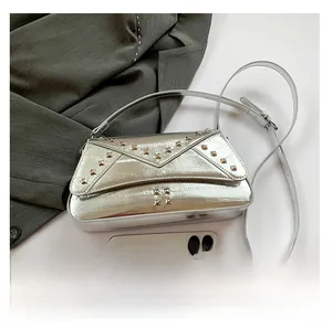 Silver square bag with metal rivets shown next to a smartphone for size comparison