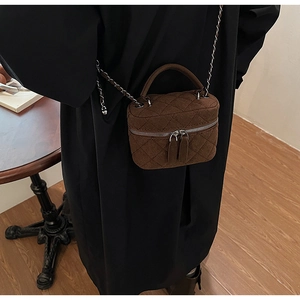 Detail of dark brown quilted mini crossbody bag with silver chain and dual zippers