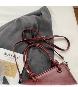 Detail of wine red bucket bag showing knotted handle and adjustable leather shoulder strap