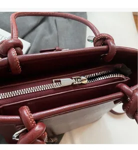 Close-up of smooth silver zipper and knotted handle detail on dark red leather bucket bag