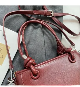 Detail of burgundy leather bucket bag with top handles, knotted accents and silver hardware