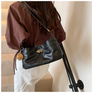 Detail of black PU leather shoulder bag featuring a gold metal lock and cross strap design