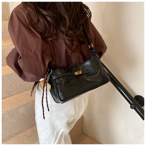 Detail of black PU leather shoulder bag featuring a gold twist lock and a decorative charm
