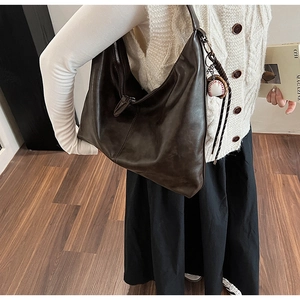 Deep brown matte leather tote bag detail with baseball pendant and braided rope