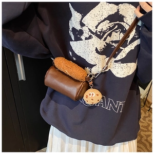 Détail d'un sac bandoulière cylindrique marron foncé avec charme biscuit sur un mannequin
