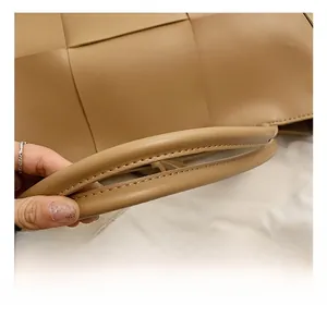 Close-up of khaki woven leather tote bag featuring thick rounded handles and fine stitching
