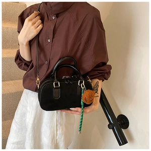 Détail du sac Boston noir mat avec breloque boule en peluche et bandoulière