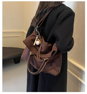Détail d'un grand sac cabas en daim marron avec un pendentif de baseball et une bandoulière
