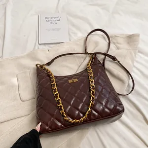 Detail of dark burgundy quilted saddle bag with gold chain and twist lock on a desk