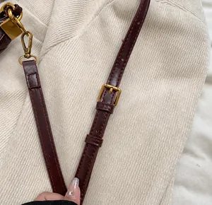 Detail of dark burgundy leather shoulder strap with adjustable golden metal buckles