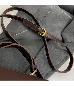 Detail of adjustable dark brown leather shoulder strap with golden metal buckle