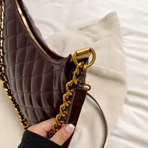 Detail of burgundy quilted leather bag with gold chain strap and metallic hardware