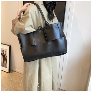 Detail view of a large black woven leather tote bag shown on model with shoulder strap