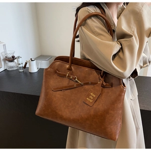 Detail view of brown vintage tote bag featuring gold buckle straps and brand tag