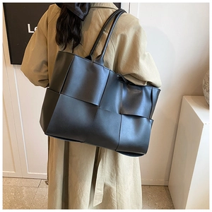 Model view of a black large woven leather tote bag paired with a stylish khaki trench coat