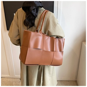 Detailed view of caramel woven tote bag on shoulder showing large leather weave pattern