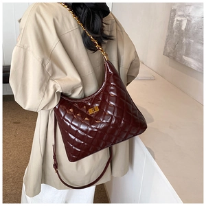 Detail of dark burgundy quilted saddle bag with gold hardware worn on shoulder
