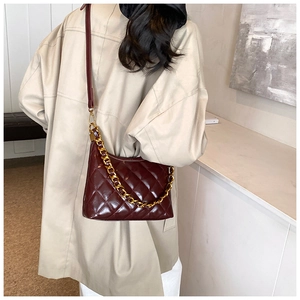 Detail of burgundy quilted crossbody bag with a thick gold chain strap on a model