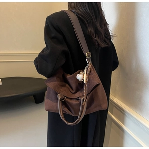Detail of a large brown suede tote bag with a baseball charm and tassel decoration