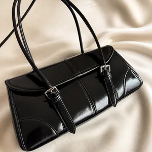 Dettaglio borsa a spalla in pelle cerata nera lucida con cinturini decorativi