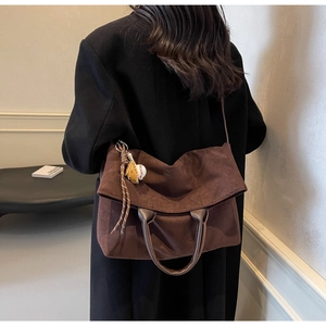 Sac cabas en daim marron avec pendentif de baseball porté à l'épaule dans un décor épuré
