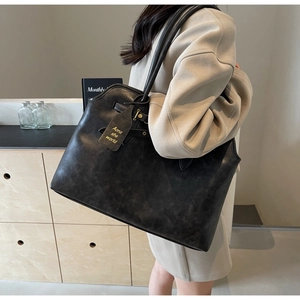 Detail view of large black leather tote bag with vintage texture and metal side buckle