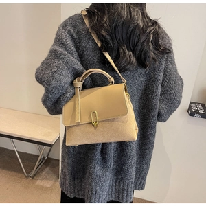 Detailed view of khaki suede and leather bag with gold ring buckle on grey sweater
