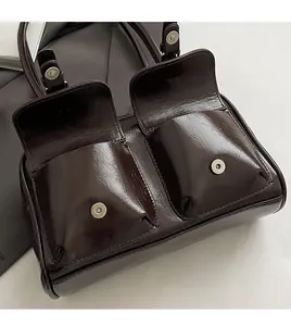 Close-up of deep brown oil wax leather pillow bag featuring dual front flap pockets with metal buckles