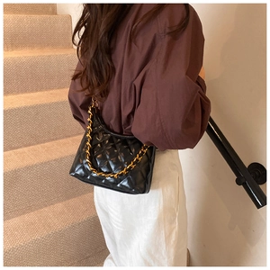 Detail of a black quilted hobo bag featuring a gold chain strap on a female model