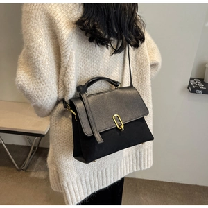Detail of elegant black leather handbag with a signature golden oval buckle and suede panels