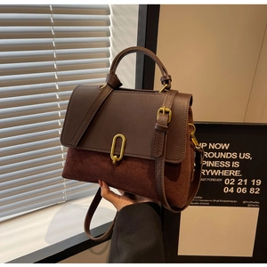 Detailed close-up of dark brown leather handbag with gold oval buckle and suede texture